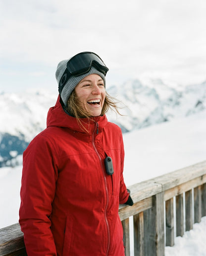 Laughing skier on a mountain terrace with a small Alpyn camera clipped to her red jacket