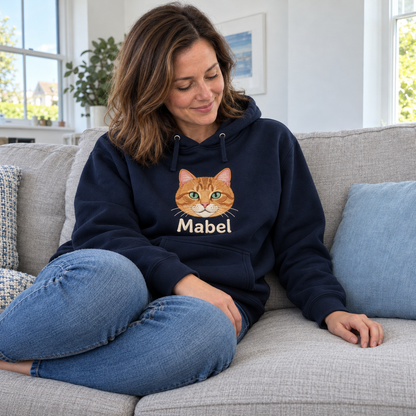 Woman on a sofa wearing a French Navy hoodie embroidered with her ginger cat Mabel